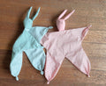 Two soft toy animals, one green and one pink, on a wooden surface.