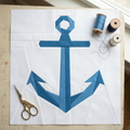 Blue anchor design on white fabric with scissors and thread spools on a wooden surface