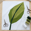 Green leaf fabric design on white paper with sewing tools on a wooden surface