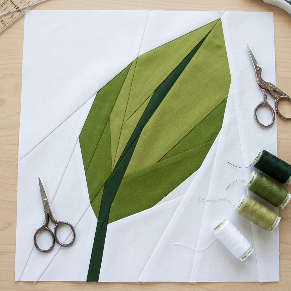 Green leaf fabric design on white paper with sewing tools on a wooden surface