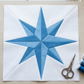 Blue star design on white paper with scissors and thread spools on a wooden surface.