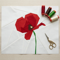 Red paper flower with green stem on a white square, surrounded by spools of thread and a pair of scissors.