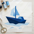 Quilt block with blue sailboat design, spools of thread, and scissors on a light wooden surface