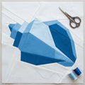 Blue geometric quilt block with scissors and thread on a white background