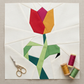 Colorful tulip-shaped quilt block with sewing tools on a beige background